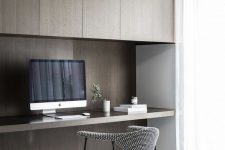 a refined minimalist home office with dark stained sleek cabinets, a built-in desk, a grey chair and a large window for more natural light