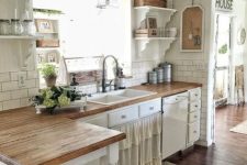 a rustic shabby chic kitchen with a ruffled curtain on a cabinet, metal and wooden pendant lamps and green blooms