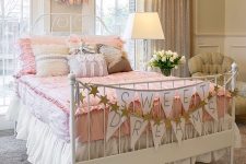 a shabby chic kid’s bedroom with tan walls, vintage furniture, pink and white bedding, garlands and bannets and sparkling curtains