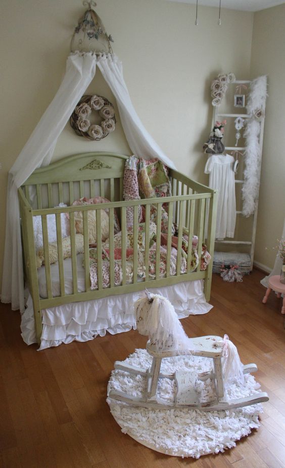 a shabby chic kid's room with light green walls, a green crib with a canopy, floral bedding, a ladder for storage, fabric flowers and vintage toys