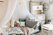 a shabby chic meets boho kid’s room with neutral walls, white vintage furniture, pretty bright bedding and pillows and a canopy over the bed
