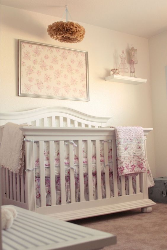 a shabby chic nursery with neutral walls and furniture, floral bedding and textiles and a paper fluff chandelier