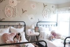 a shabby chic shared bedroom with a floral statement wall, metal beds, pink bedding, a refined nightstand and a crystal chandelier