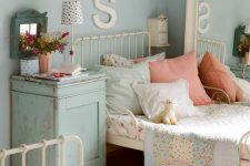 a shabby chic shared kids’ bedroom with white metal beds, a large mirror, a blue nigthstand and pretty floral bedding