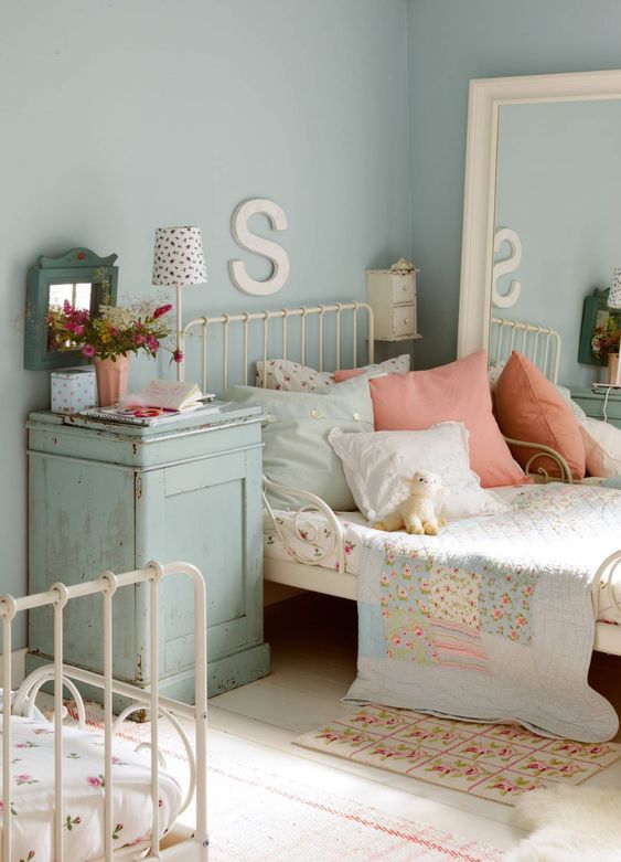 a shabby chic shared kids' bedroom with white metal beds, a large mirror, a blue nigthstand and pretty floral bedding