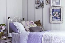 a shabby farmhouse bedroom in white, with a forged bed, a crate nightstand, some vintage suitcases and a gallery wall