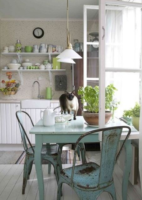 a simple shabby chic kitchen with white beadboard cabinets, light blue shabby furniture, green touches and potted greenery