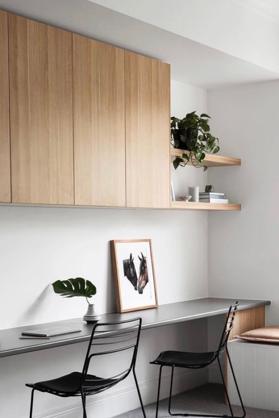 a sleek minimalsit home office with a sleek storage unit and built-in shelves, a floating desk, black chairs and a windowsill bench