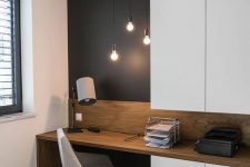 a small and functional home office with a black accent wall, sleek white storage units, a built-in desk and a white chair plus bulbs hanging