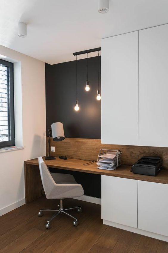 a small and functional home office with a black accent wall, sleek white storage units, a built-in desk and a white chair plus bulbs hanging