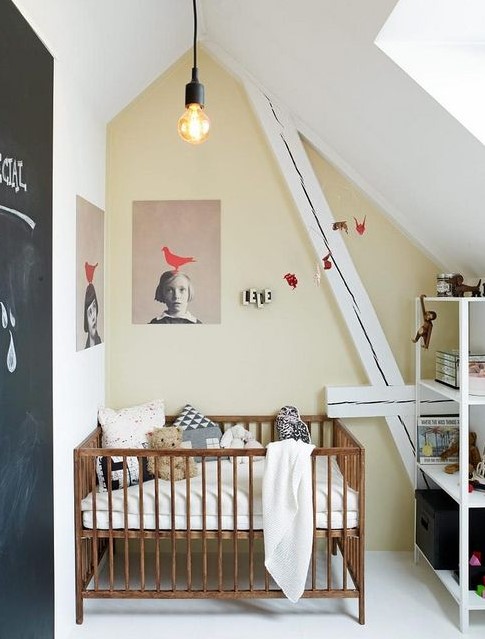 a small attic nursery with a catchy artwork, a chalkboard door, a simple crib and a storage unit for a modern look