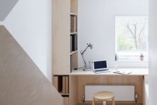 a small minimalist home office nook with a view, a built-in plywood storage unit, a built-in desk and a stool is chic and comfortable