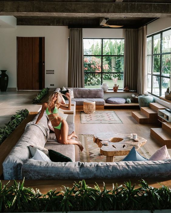 a stylish modern conversation pit with several sofas, ldders and benches, tree slice coffee tables and lots of pillows