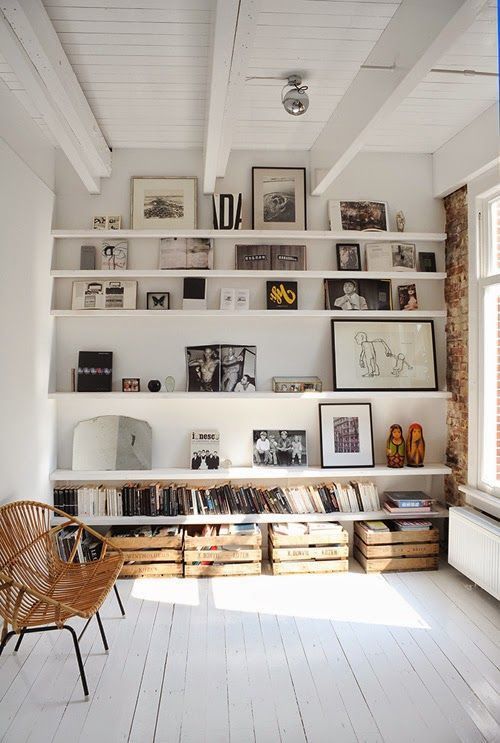 a stylish nook with white ledges that display artworks, photos and are used as bookshelves, crates for storage under them