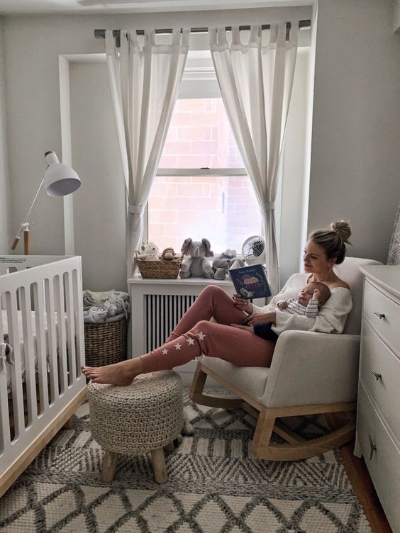 a tiny and cozy baby nursery with a white crib, a white rocker, a pouf and a basket for textiles plus toys