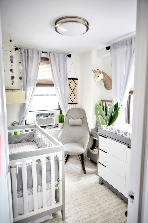 a tiny and lovely nursery in neurrals, with a stylish crib and dresser, a grey chair, some neutral bedding and faux taxidermy