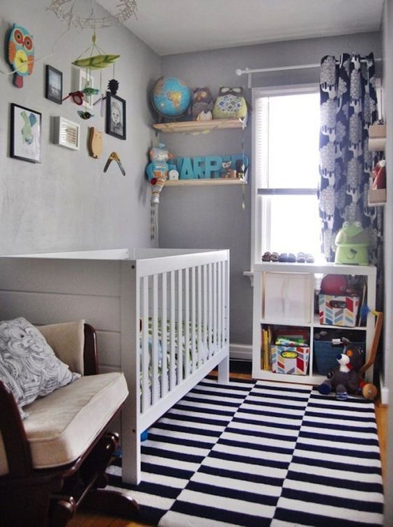 a tiny colorful nursery with grey walls, a white crib, a printed rug and curtains, a white storage unit and a white rocker chair