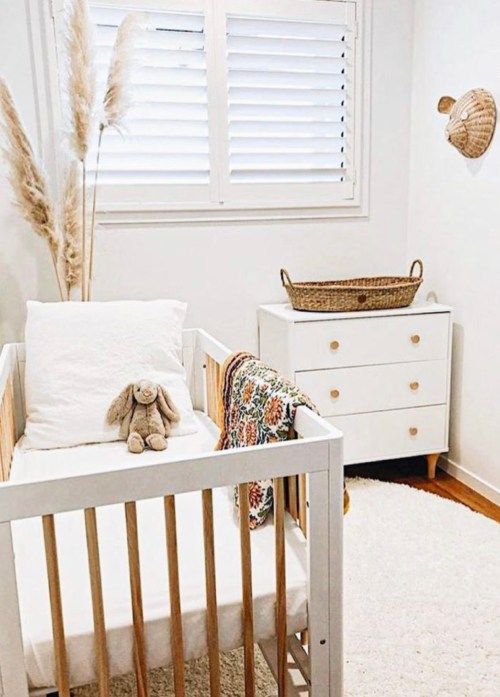 a tiny neutral nursery with a white crib and a dresser that is a changing table, pampas grass, layered rugs