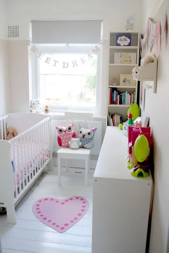 a tiny neutral nursery with white furniture, a built-in bookshelf and a dresser, a banner, some bright textiles and colorful toys