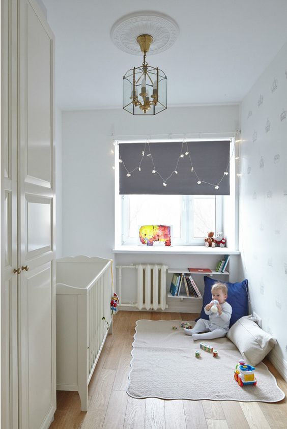a tiny nursery with a white vintage crib, a windowsill as a table, soem bookshelves and a play space on the floor