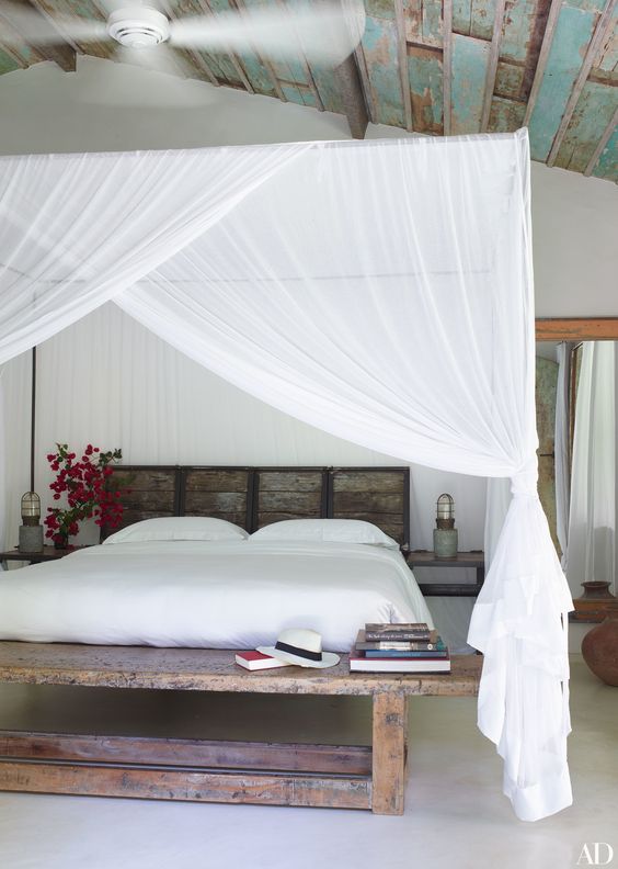 a tropical bedroom with a pallet bed and bench plus mosquito net canopies and curtains