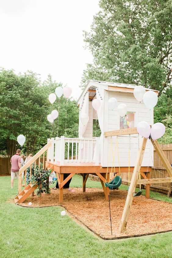 a white kids' playhouse with a porch, a ladder, swings and white balloons is a lovely idea for your garden