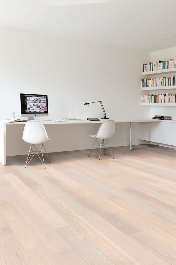 a white minimalist home office with bookshelves, a long desj and white chairs plus a black table lamp is a cool space