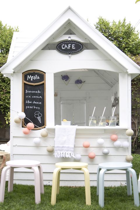a white planked playhouse with a chalkboard and a sign, with a bar and some pastel stools is a great idea for summer for your kids