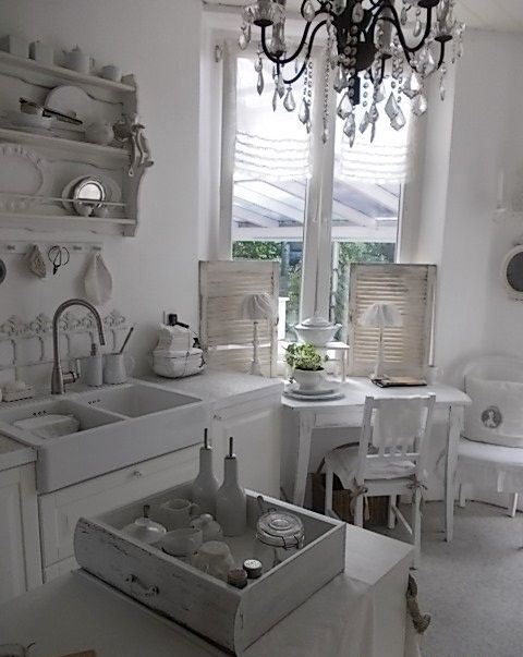 a white shabby chic kitchen with vintage cabinets, a crystal chandelier, open shelving units and shutters is chic