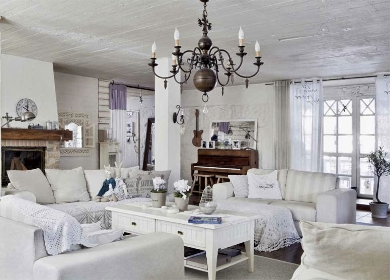a white shabby chic living room with elegant furniture, a vintage chandelier, a low table, a fireplace in stone and crochet and doilies