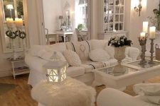 a white shabby chic living space with elegant mirrors and stylish furniture, candles, candle lanterns and white bloom