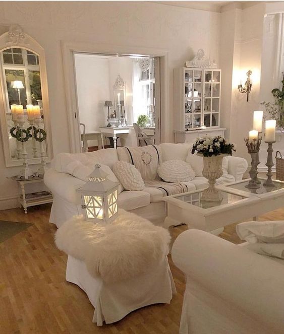 a white shabby chic living space with elegant mirrors and stylish furniture, candles, candle lanterns and white bloom