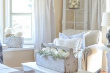 a white shabby chic space with elegant furniture, a low table, a toolbox with blooms and white pumpkins