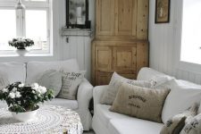 a white vintage to shabby chic living room with white sofas, a wooden wardrobe, a crystal chandelier, a black table, a crochet tablecloth and blooms