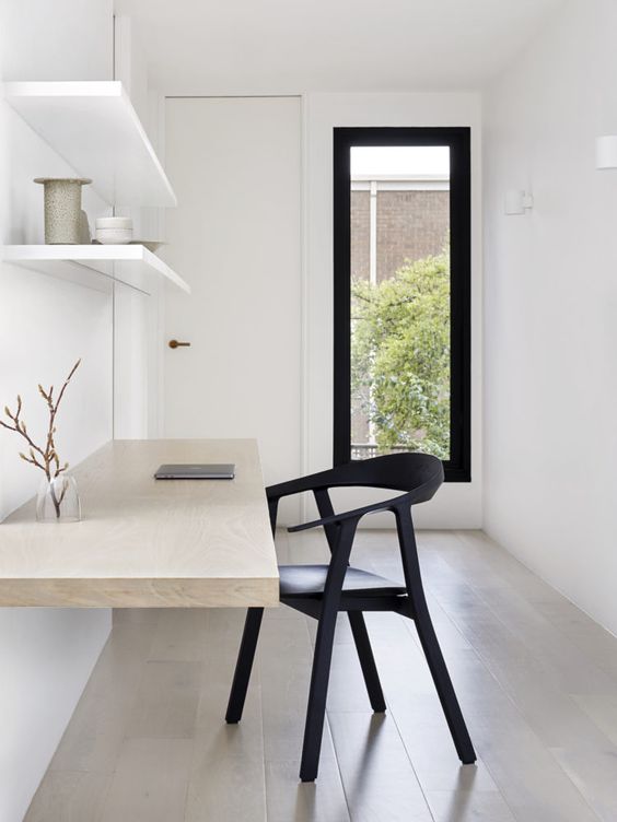an airy minimalist home office with open shelves, a floating desk, a black chair and a narrow window for a view