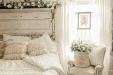 an airy white shabby chic bedroom with a shabby headboard, vintage furniture, a crystal chandelier and neutral blooms