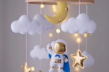 an astronaut mobile with clouds, gold stars, a half moon and lights is a unique solution for any space-themed nursery