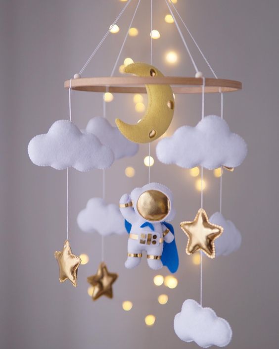 an astronaut mobile with clouds, gold stars, a half moon and lights is a unique solution for any space themed nursery