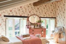 an attic shared kids’ bedroom with floral wallpaper, wooden beams, vintage furniture, pink bedding and a dresser and a pink framed mirror