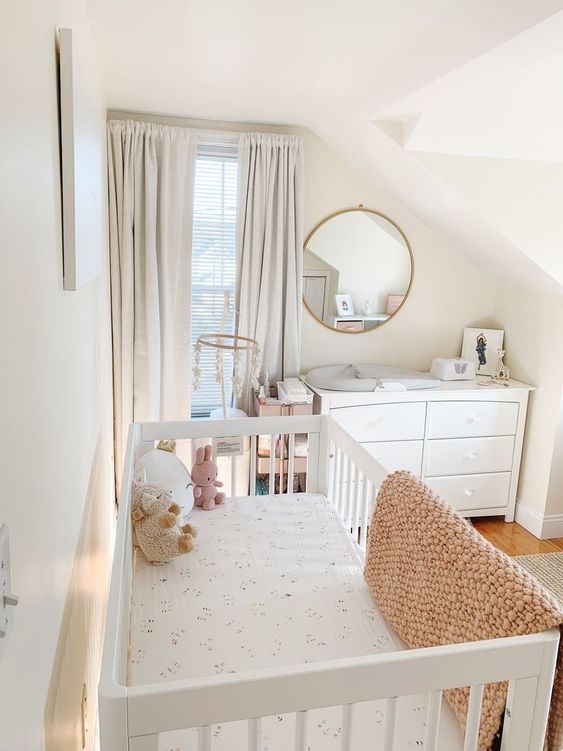 an attic tiny nursery with a white crib and a dresser that doubles as a changing table, neutral textiles and a round mirror