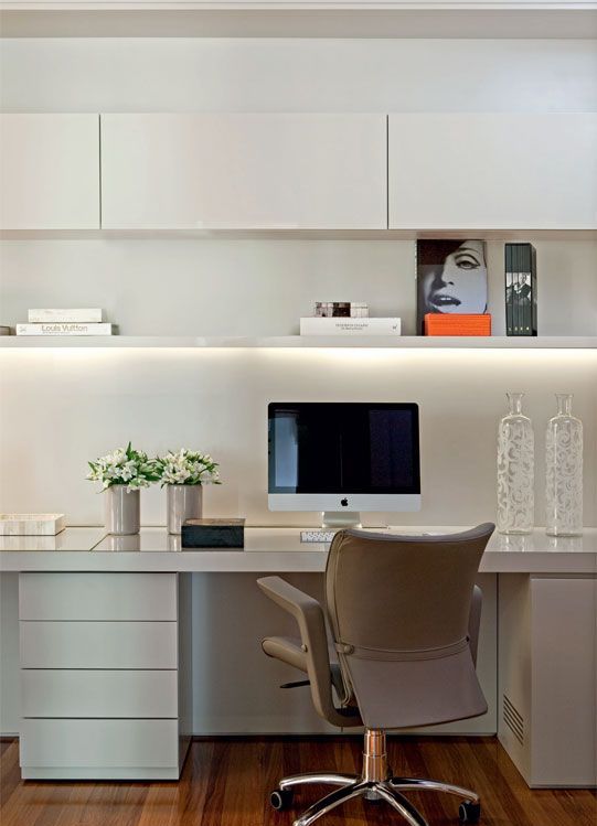 an elegant minimalist white home office with sleek cabinety, an open shelf with built in lights, a leather chair and some art