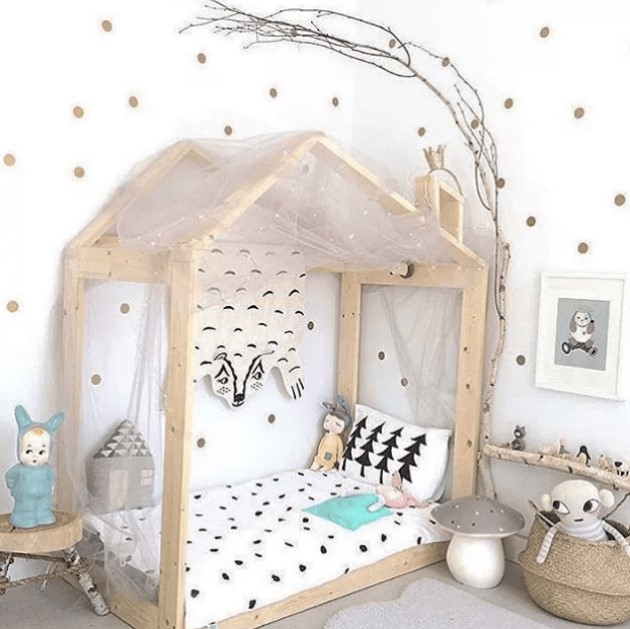 an ethereal Scandinavian kids' room with a wooden house shaped bed, a branch shelf, polka dot walls, artworks and some fun toys