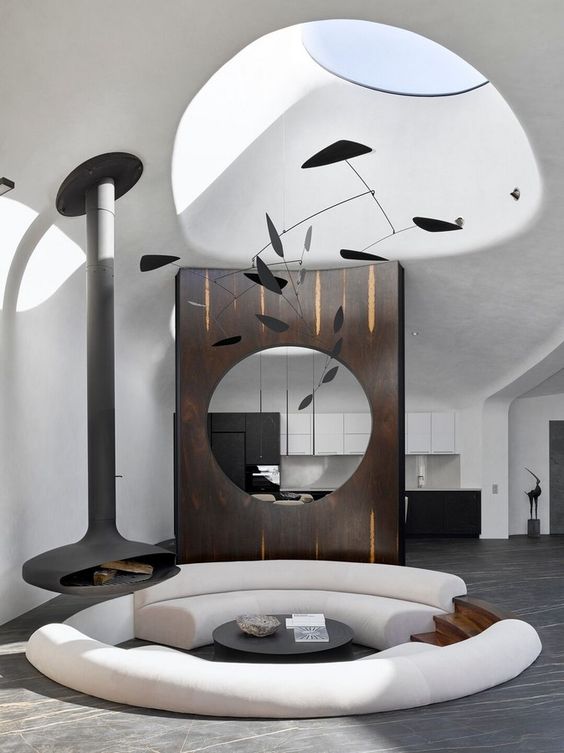 an ultra-minimalist and bold round conversation pit with white curved sofas, a black table and a suspended black fireplace