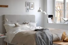a Nordic bedroom with simple and laconic furniture, a grey upholstered bed, white pendant lamps over the space