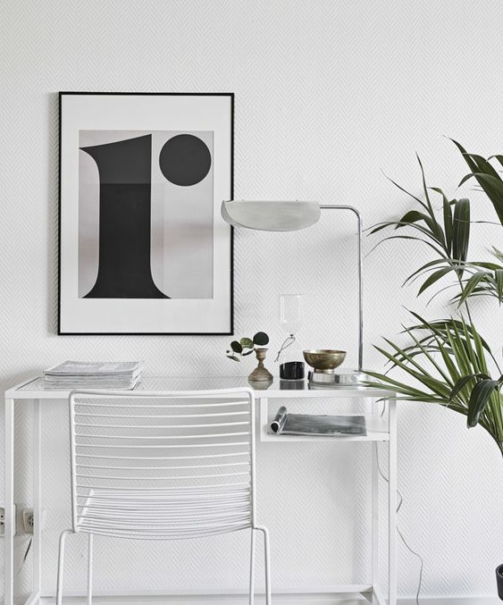 a Nordic working nook with a white Vittsjo desk, a white metal chair, a black and white artwork, a white lamp and some potted greenery
