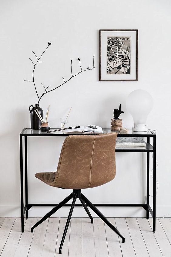 a Nordic working space with a black Vittsjo table, a tan leather chair, a black and white artwork, branches in a vase and some accessories