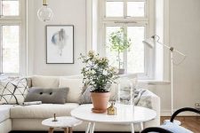 a Scandinavian living room with a large neutral sectional, a dark chair, white tables, a basket and an IKEA Ranarp floor lamp
