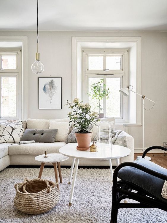 a Scandinavian living room with a large neutral sectional, a dark chair, white tables, a basket and an IKEA Ranarp floor lamp