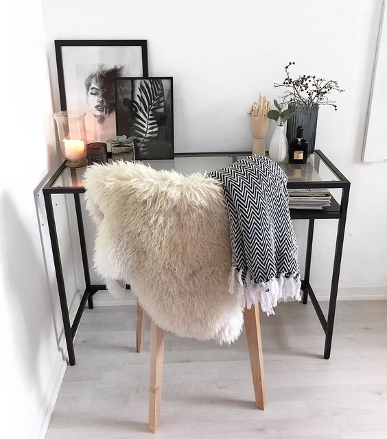 a Scandinavian working space with a black Vittsjo desk, a light-stained chair, some candles and greenery and black and white artworks