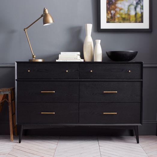 a black IKEA Malm dresser with brass handles and little knobs on tall legs is a chic mid-century modern piece of furniture